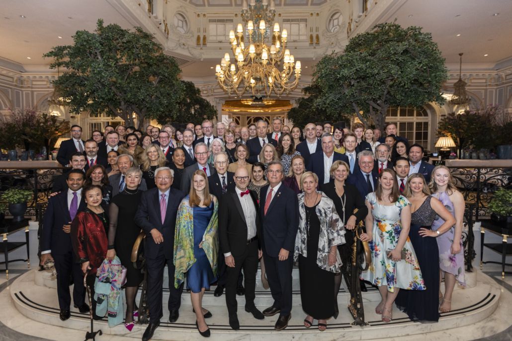 People in formal attire standing under a gold chandelier.