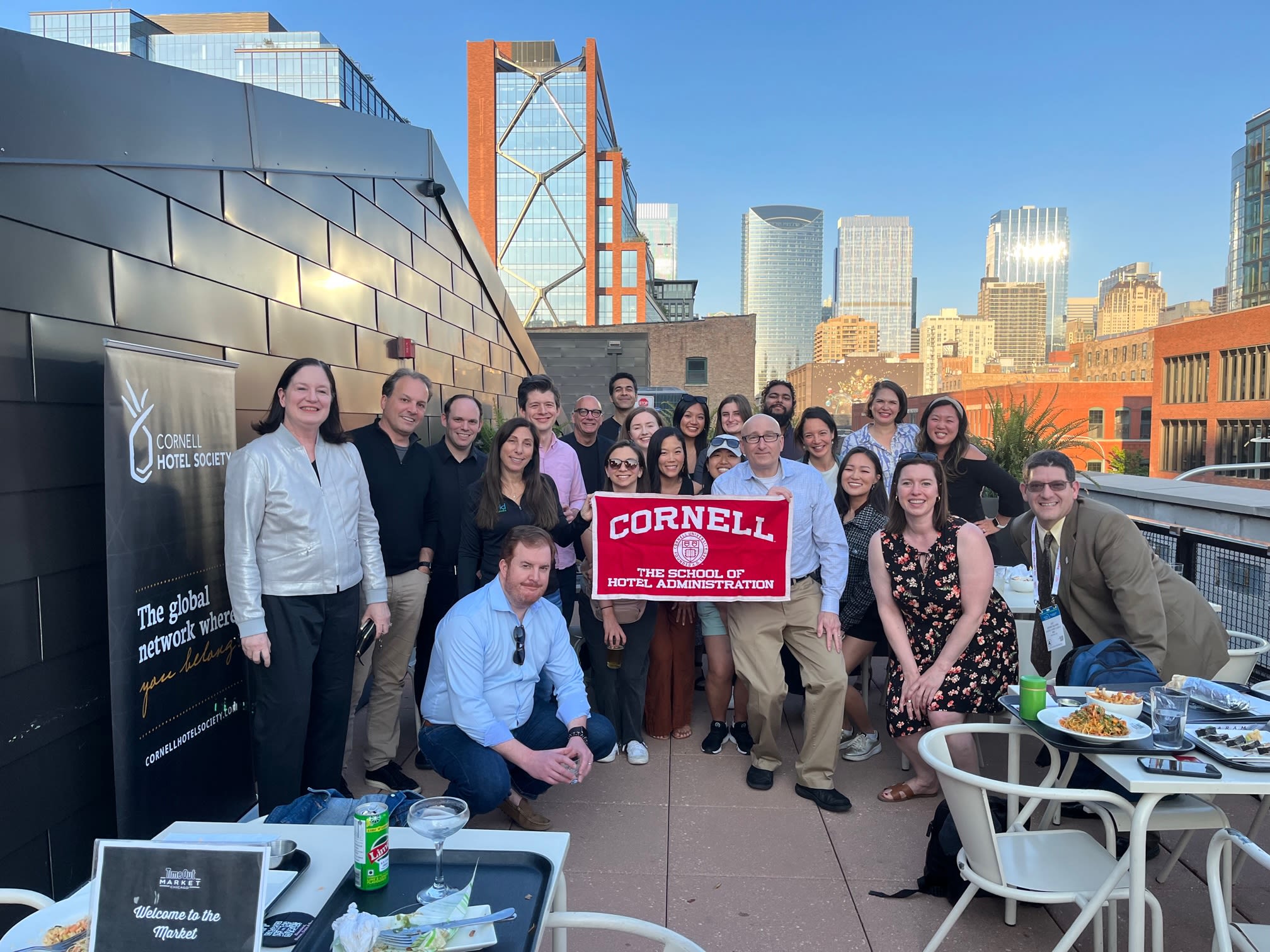 People pose on a rooftop holding a red Cornell banner.