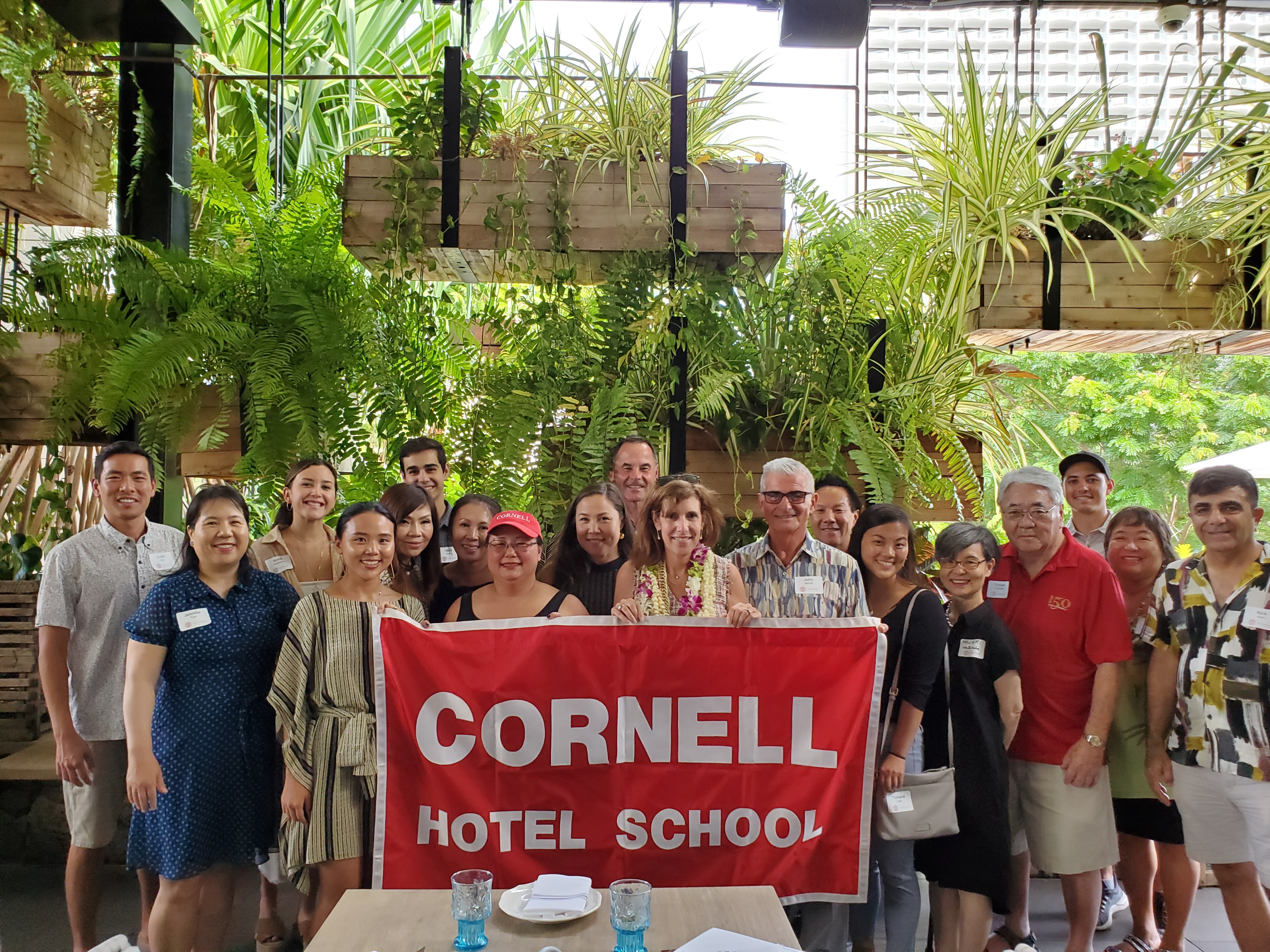 People pose with a "Cornell Hotel School" banner.