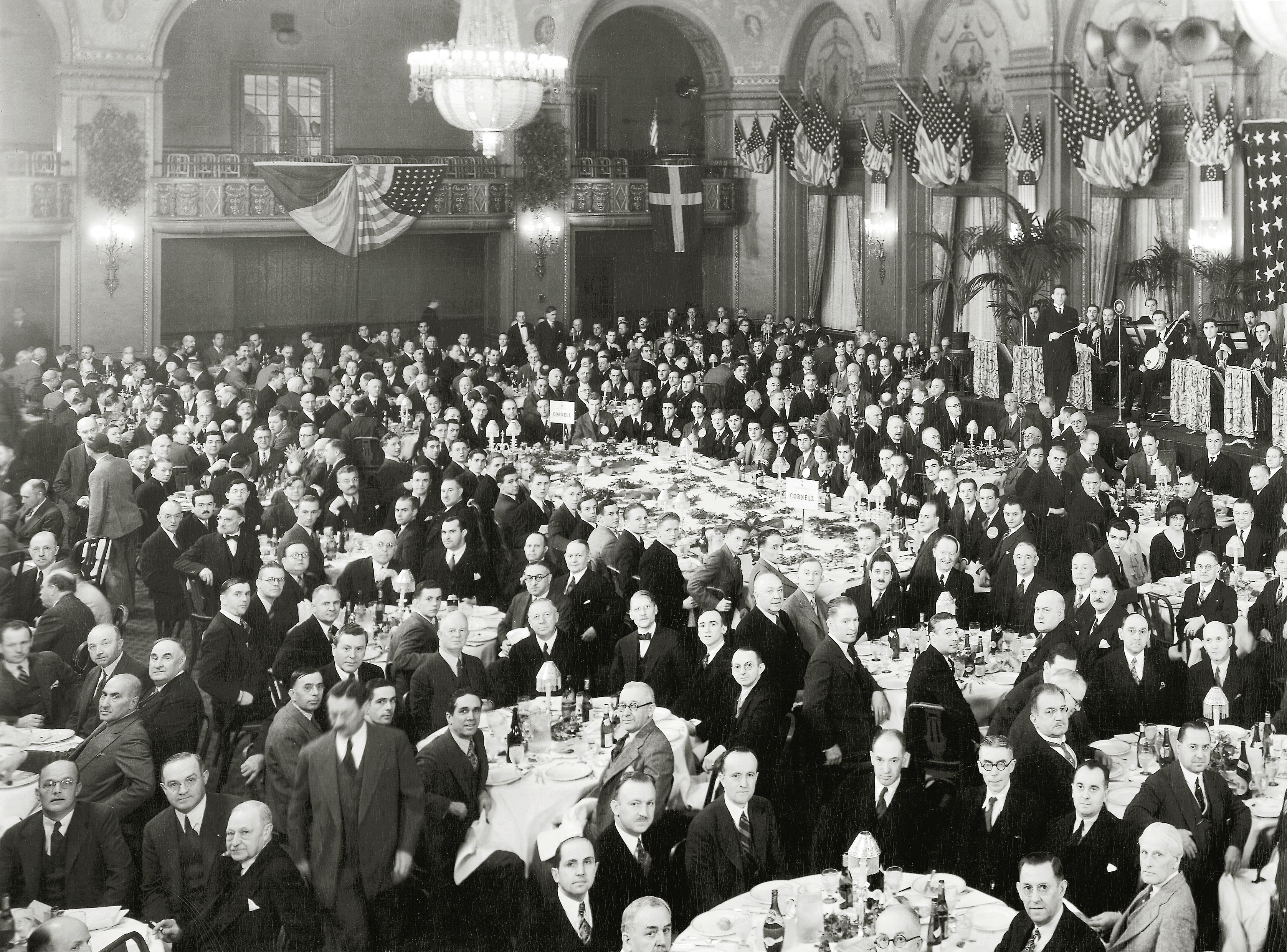 Black and white image of people in formal business attire in a grand banquet hall.
