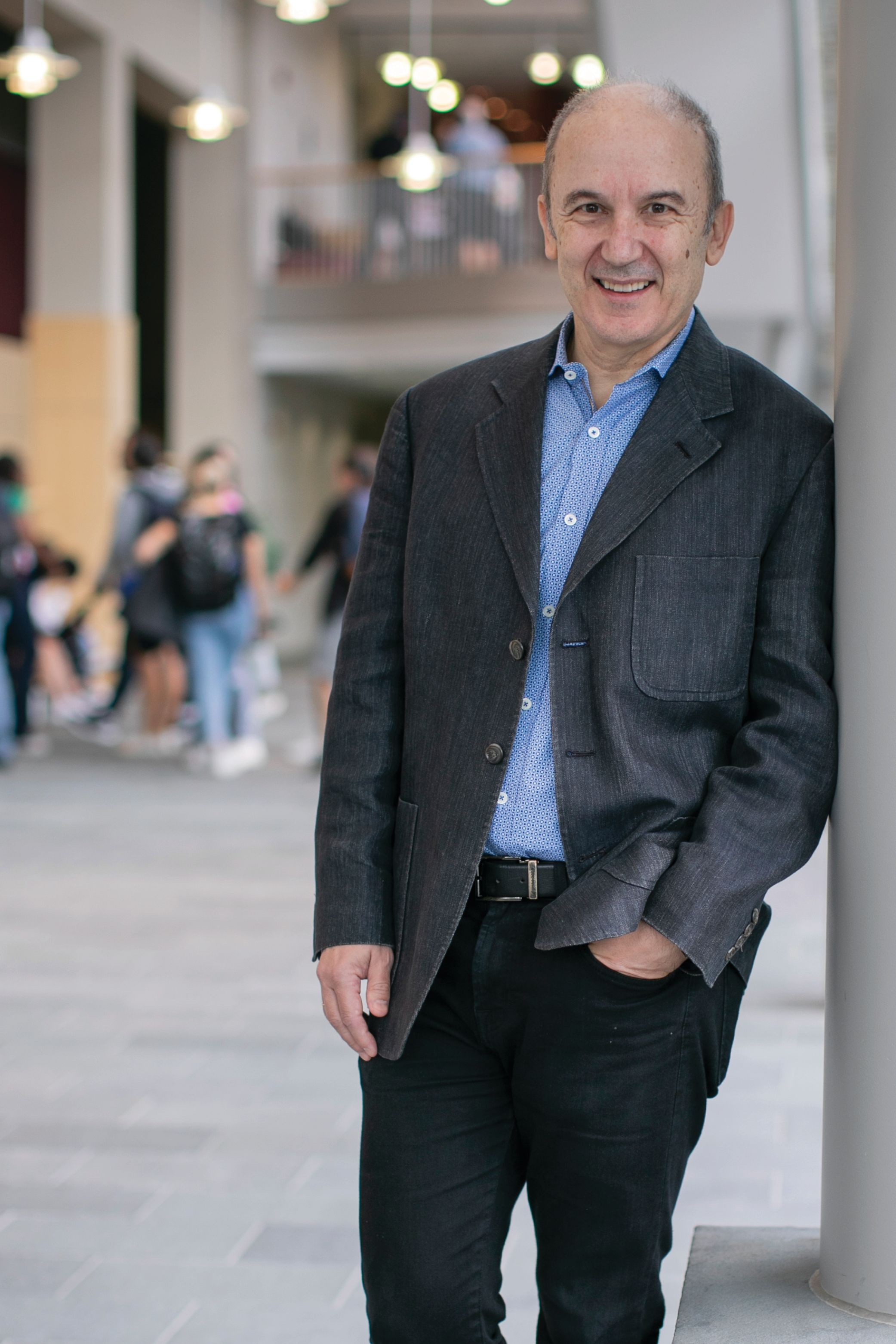 Asís Martínez-Jerez leans against a wall and smiles with one hand in his pants pocket.