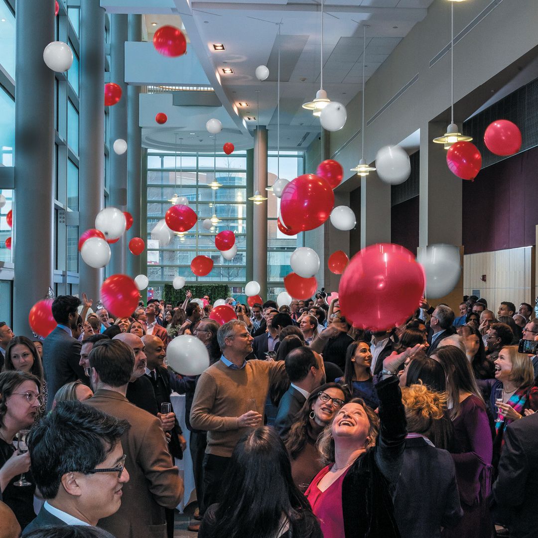 People stand and look up at red and white balloons falling from the above.