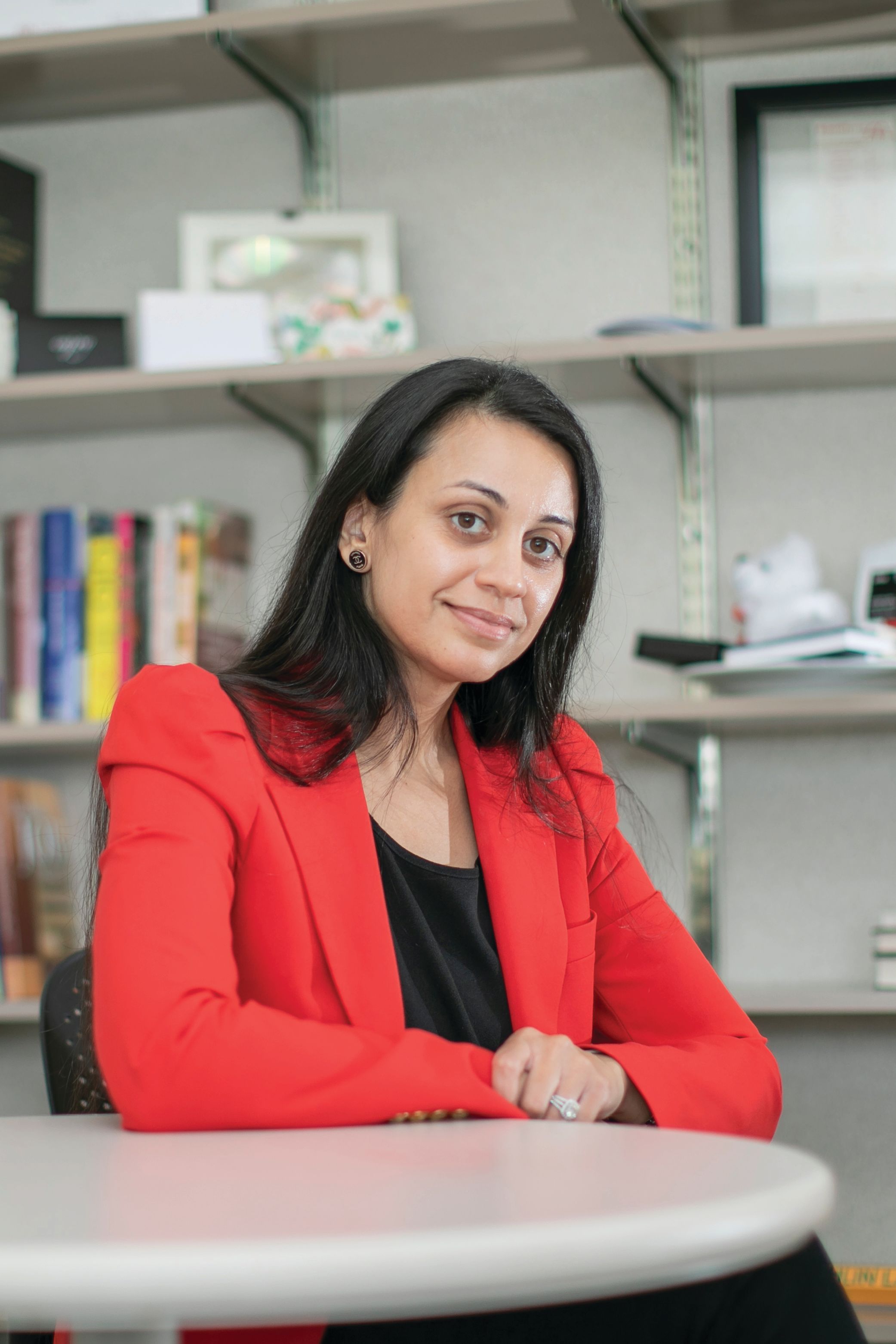 Tashlin Lakhani sits at a table in a bright red blazer and black shirt.
