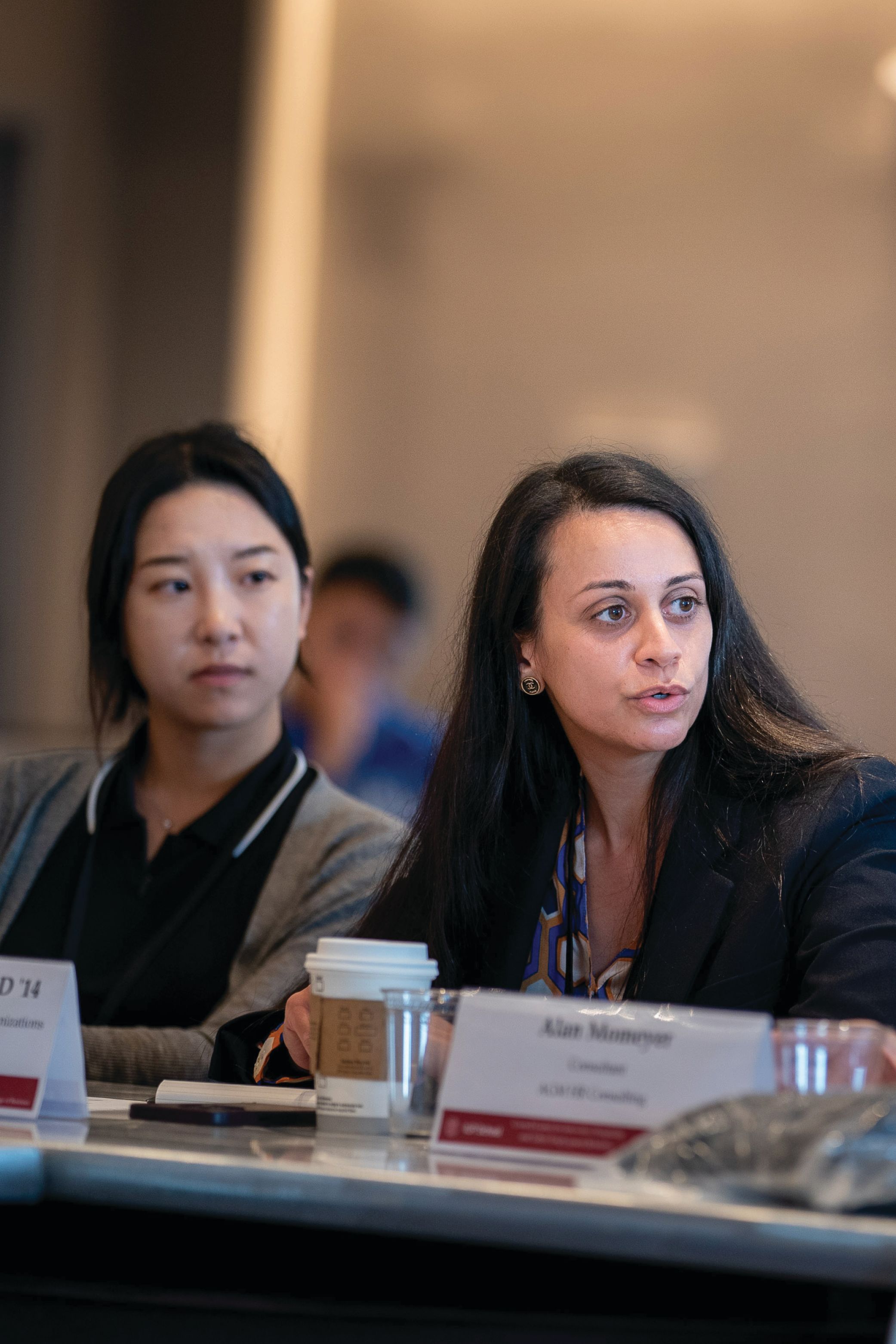 Two women sitting on at a table looking to the right.