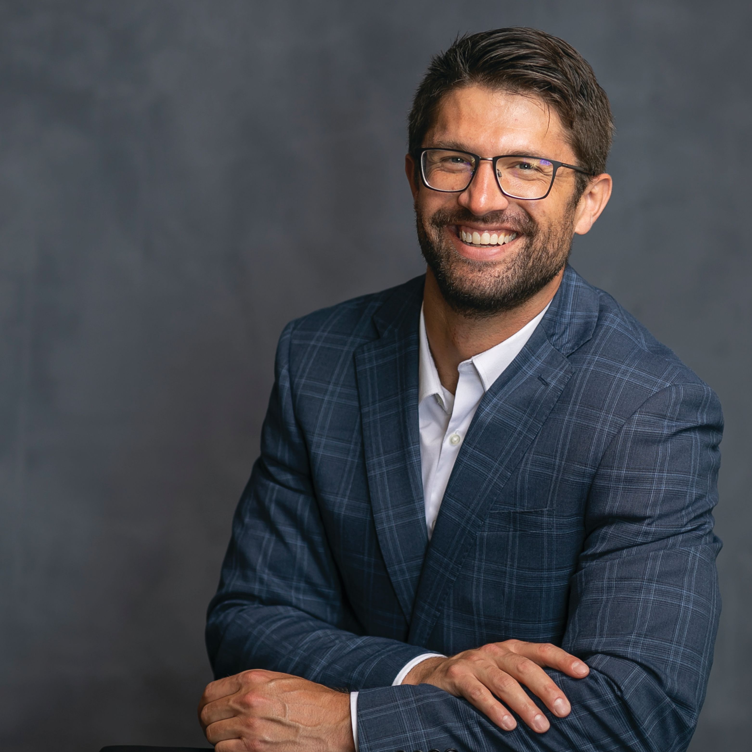 Sean Flynn smiles in a blue plaid suit jacket. 