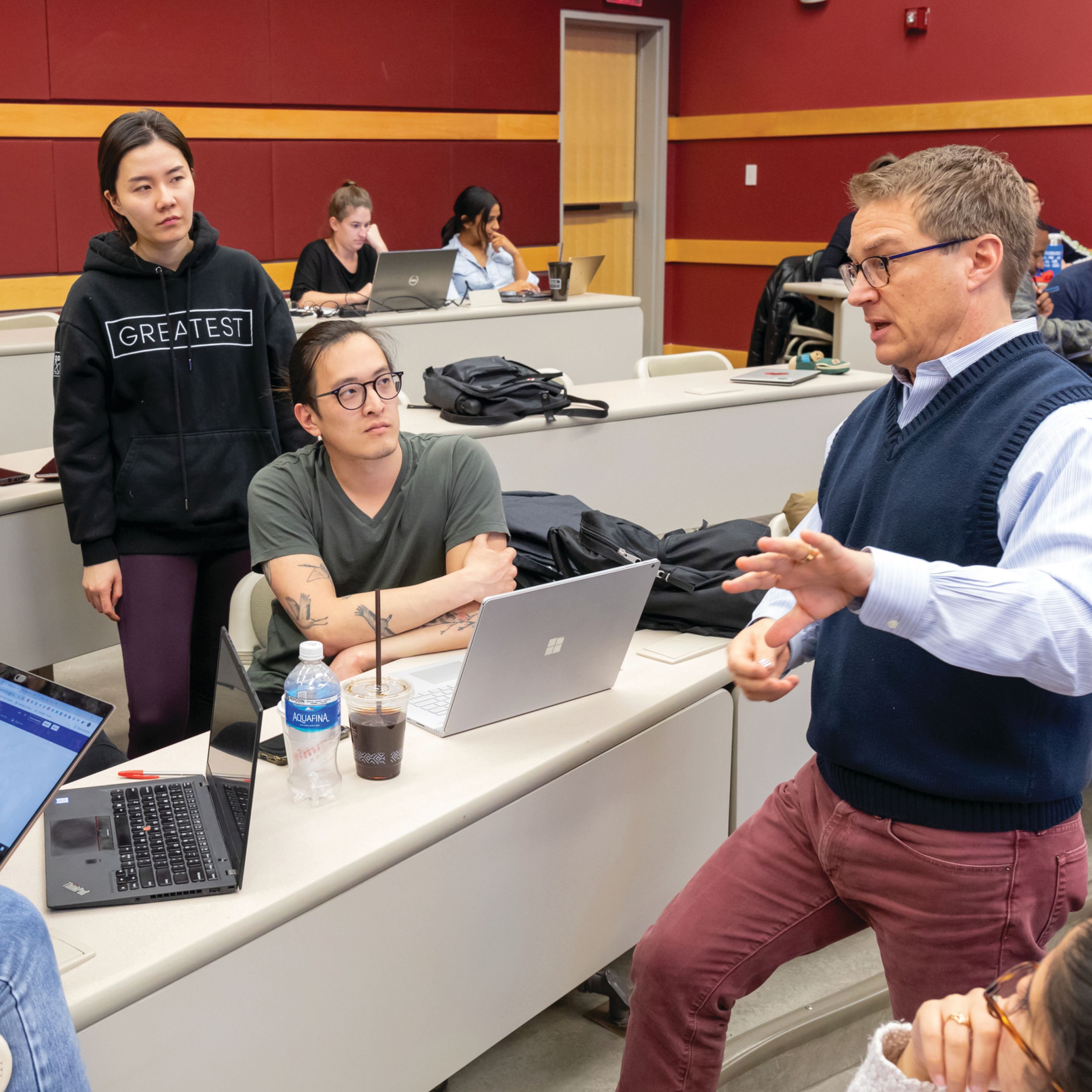 Professor Robert J. Kwortnik stands in a tiered classroom speaking to a small group of students.
