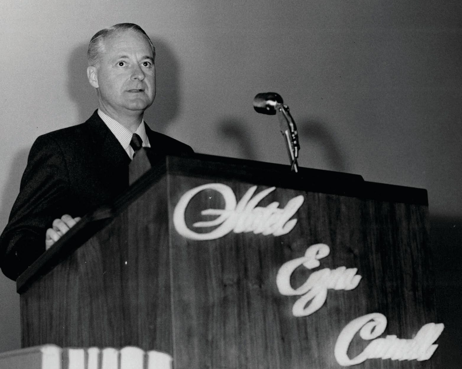 oseph P. Binns ’28 stands behind a podium that says "Hotel Ezra Cornell."