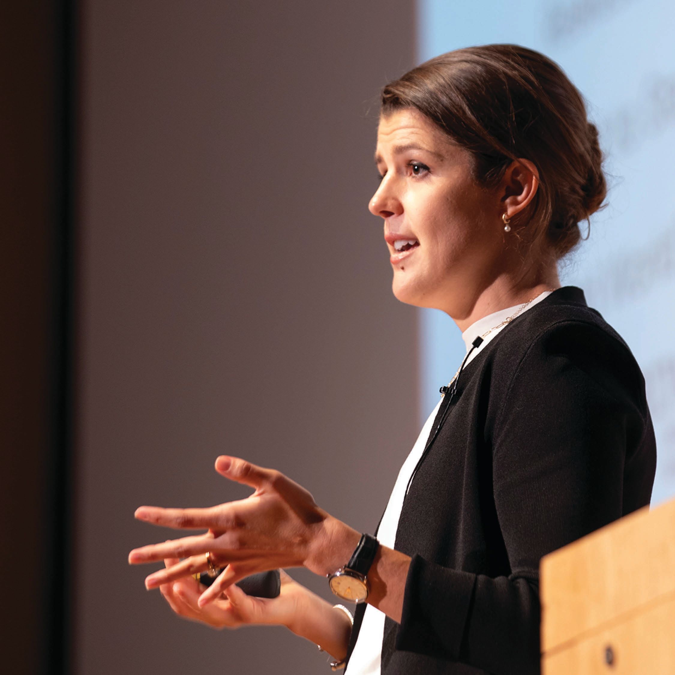 Heggie speaks next to a podium in font of a projector screen.