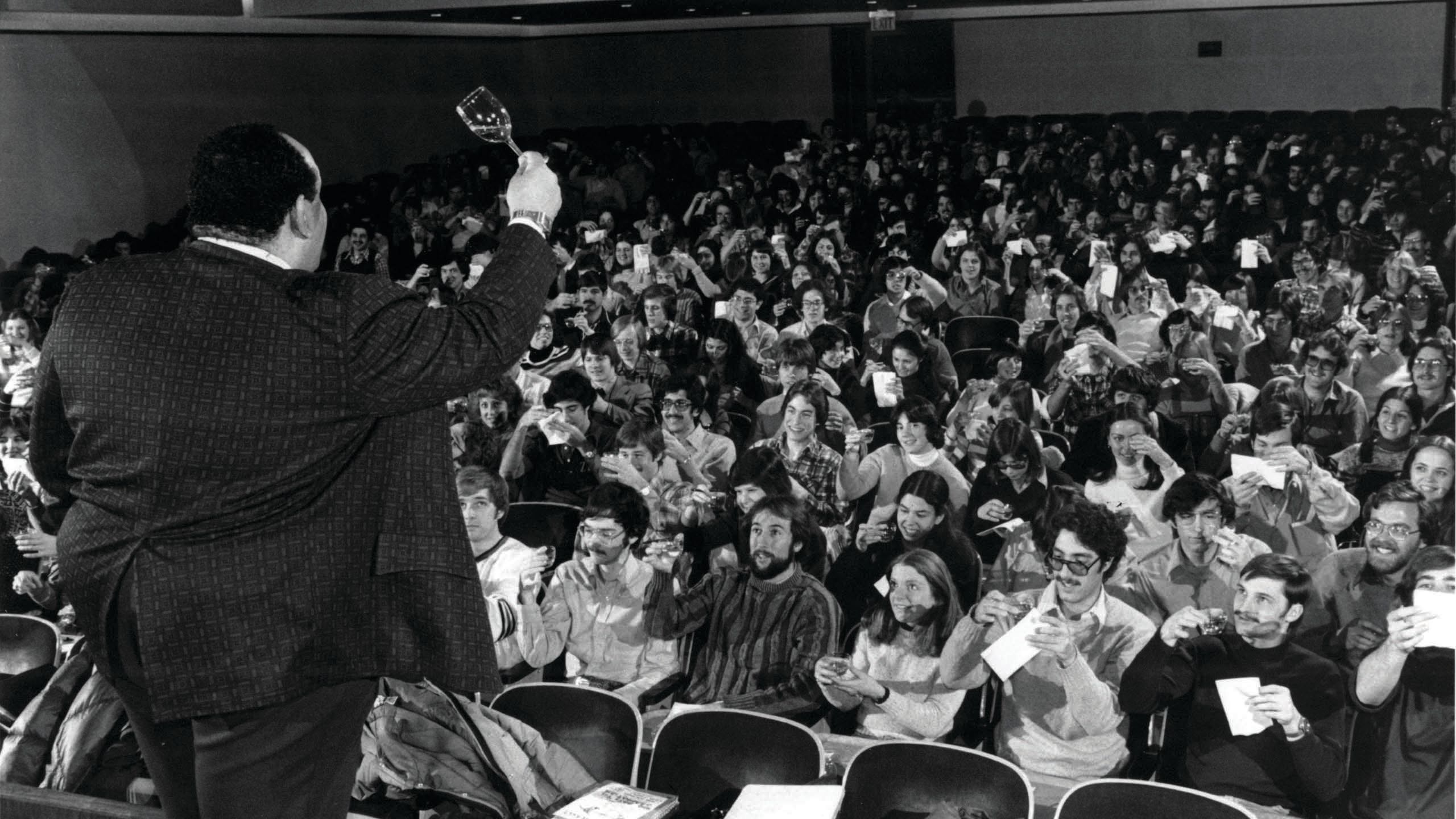 Wine professor Vance Christian holds a wine glass in front of a crowded classroom.
