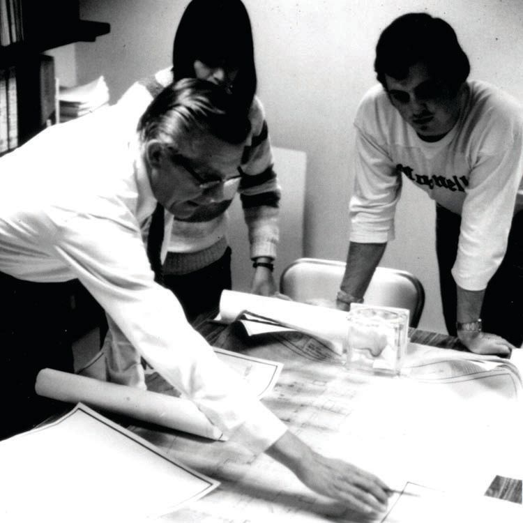 Three people review papers on a table.