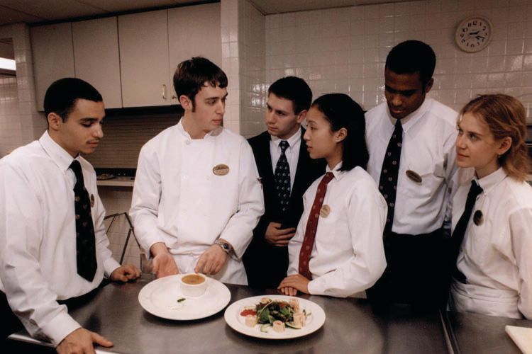Students in Banfi uniforms stand around a table with two plates.