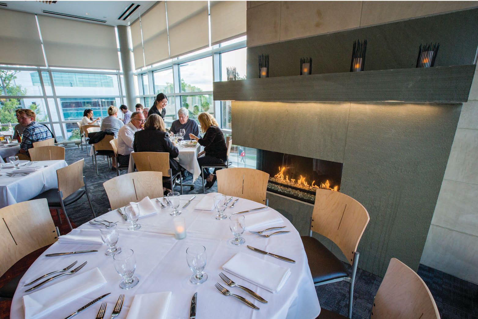 Table set with a white table cloth in front of a lit fireplace.