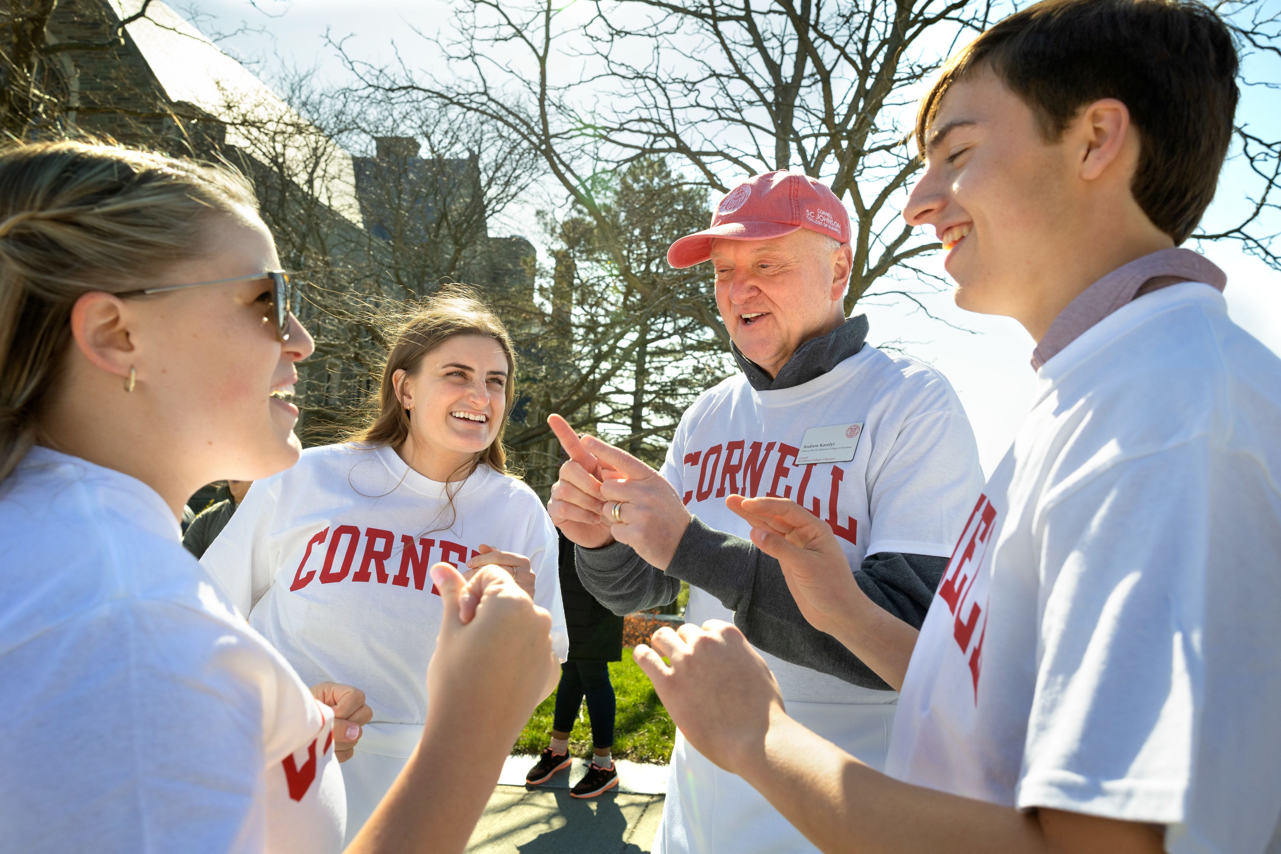 Dean Karolyi wears a white Cornell t-shirt and a red Cornell baseball hat talking to students.