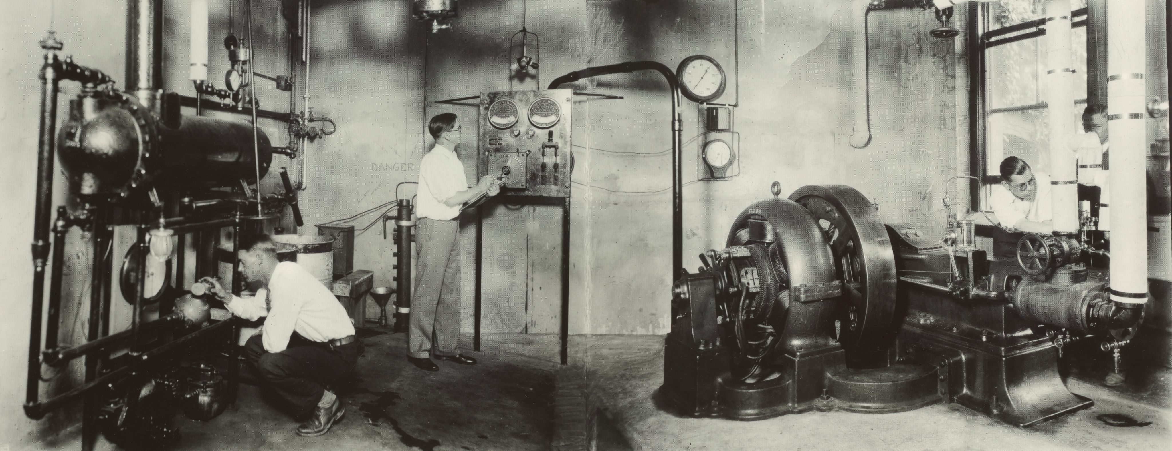 Black and white image of three male students studying machinery.