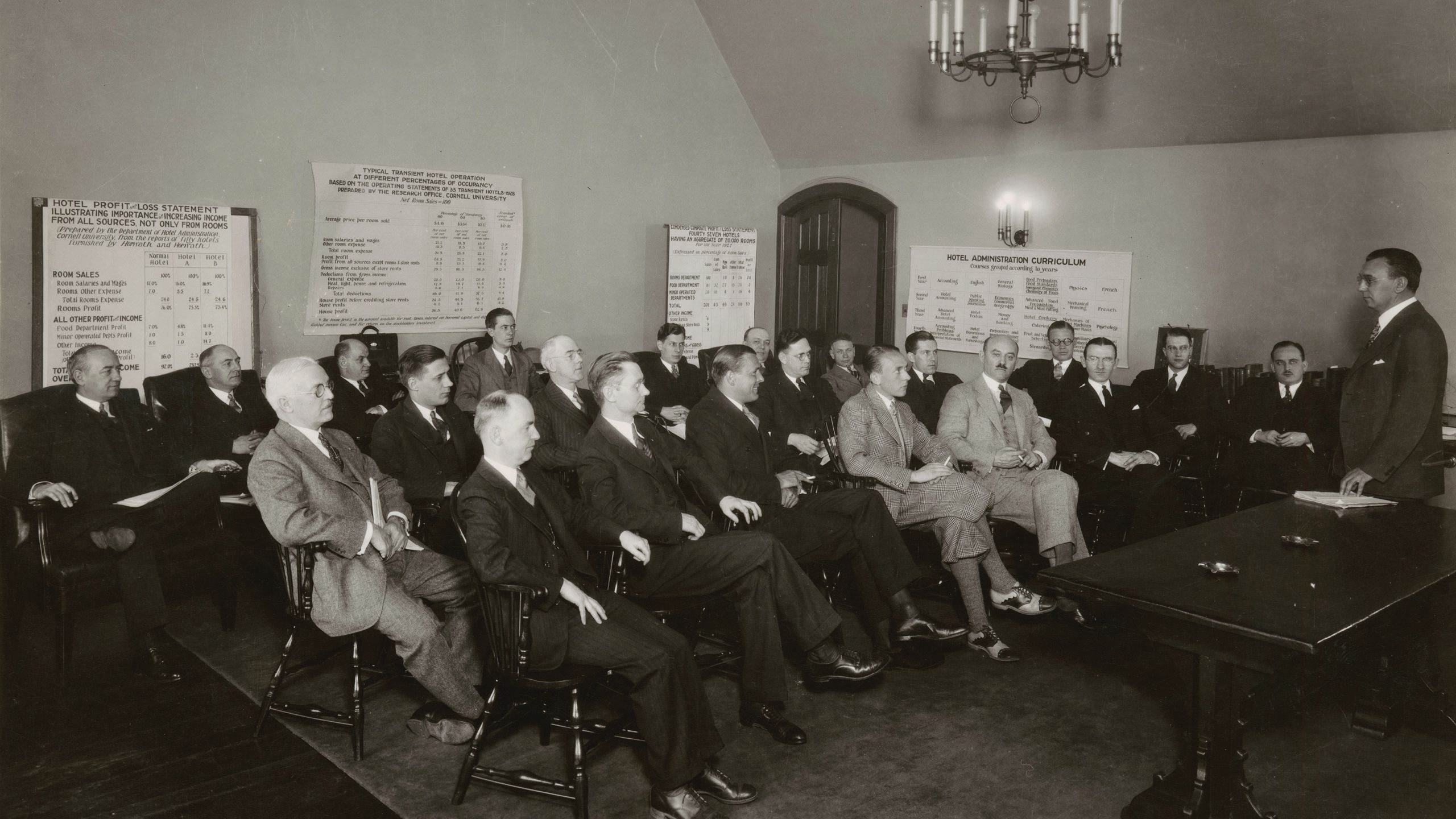 Black and white photo of men in suits sitting in wooden chairs.