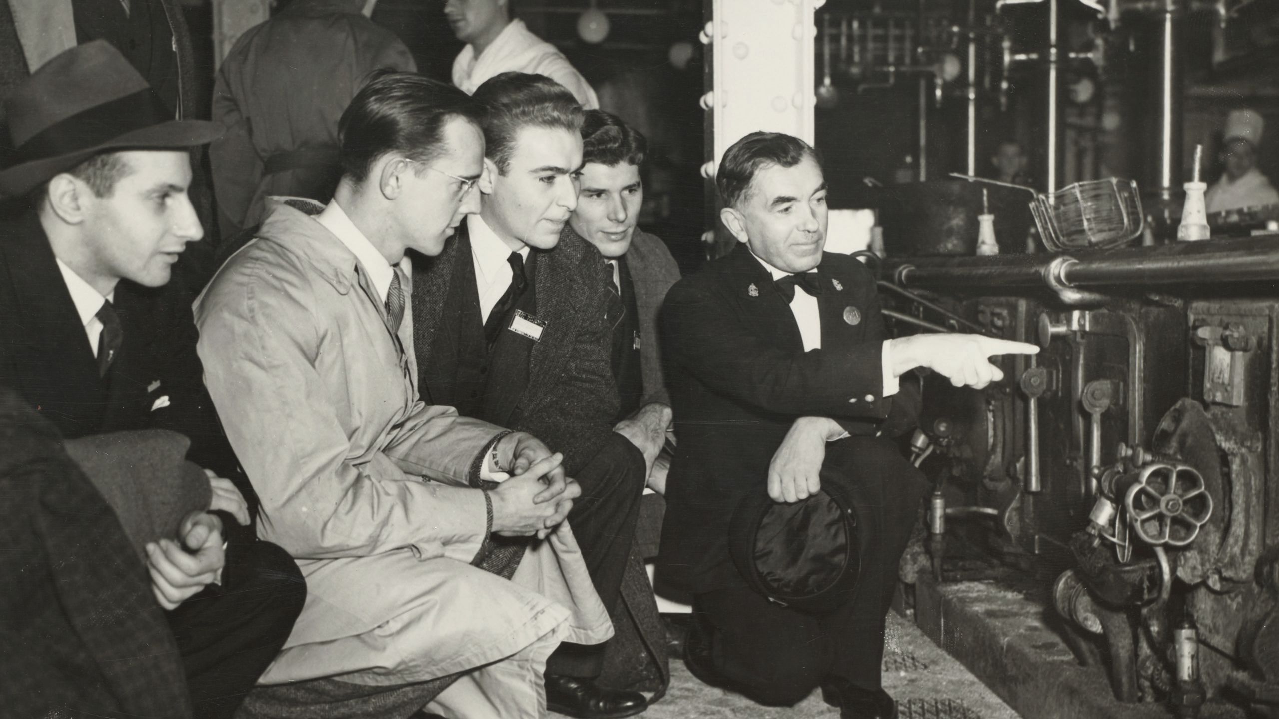 Black and white photo of men in suits crouching down to look at something. 